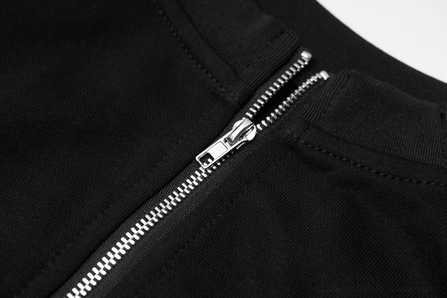 Close-up detail of silver metal dual zipper teeth with precise topstitching on black woven fabric