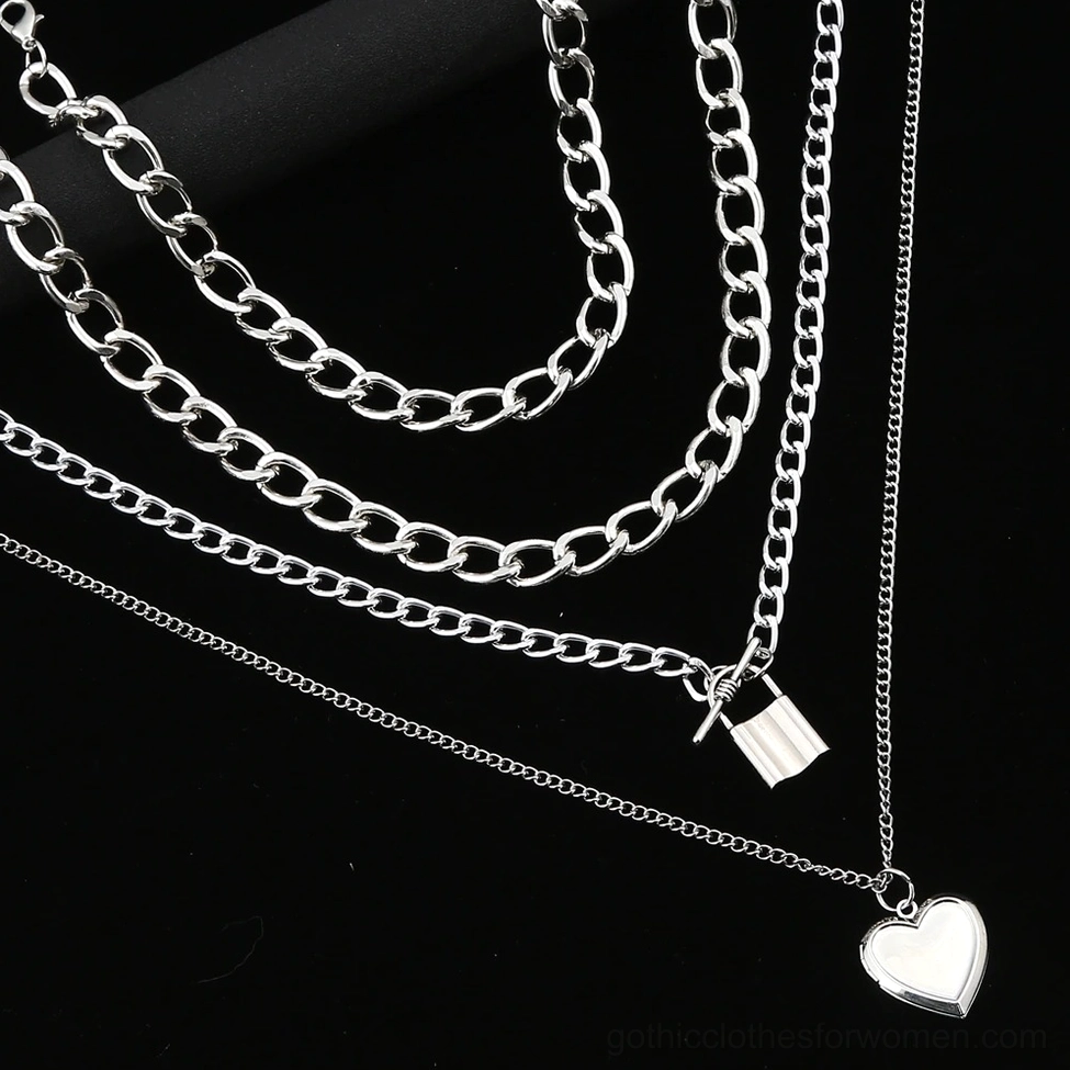 Layered gothic chain necklace with lock and heart pendants on black cylindrical display prop, close-up angled view showing chain details