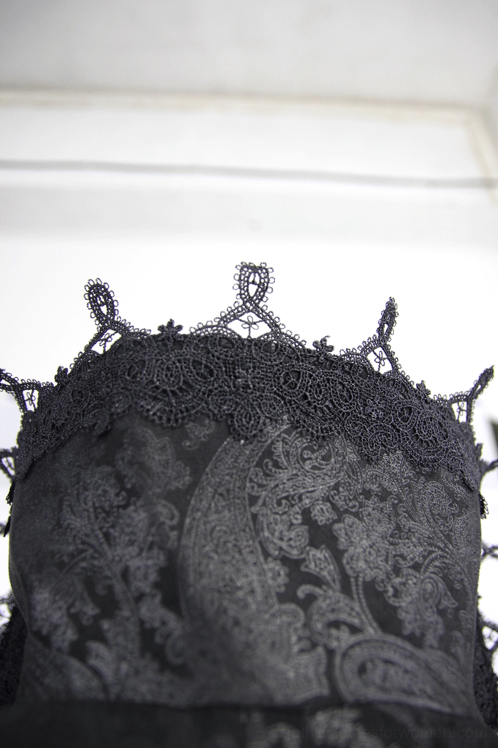 Close-up detail shot of black gothic coat fabric showing paisley jacquard pattern and ornamental lace spiked trim embellishment