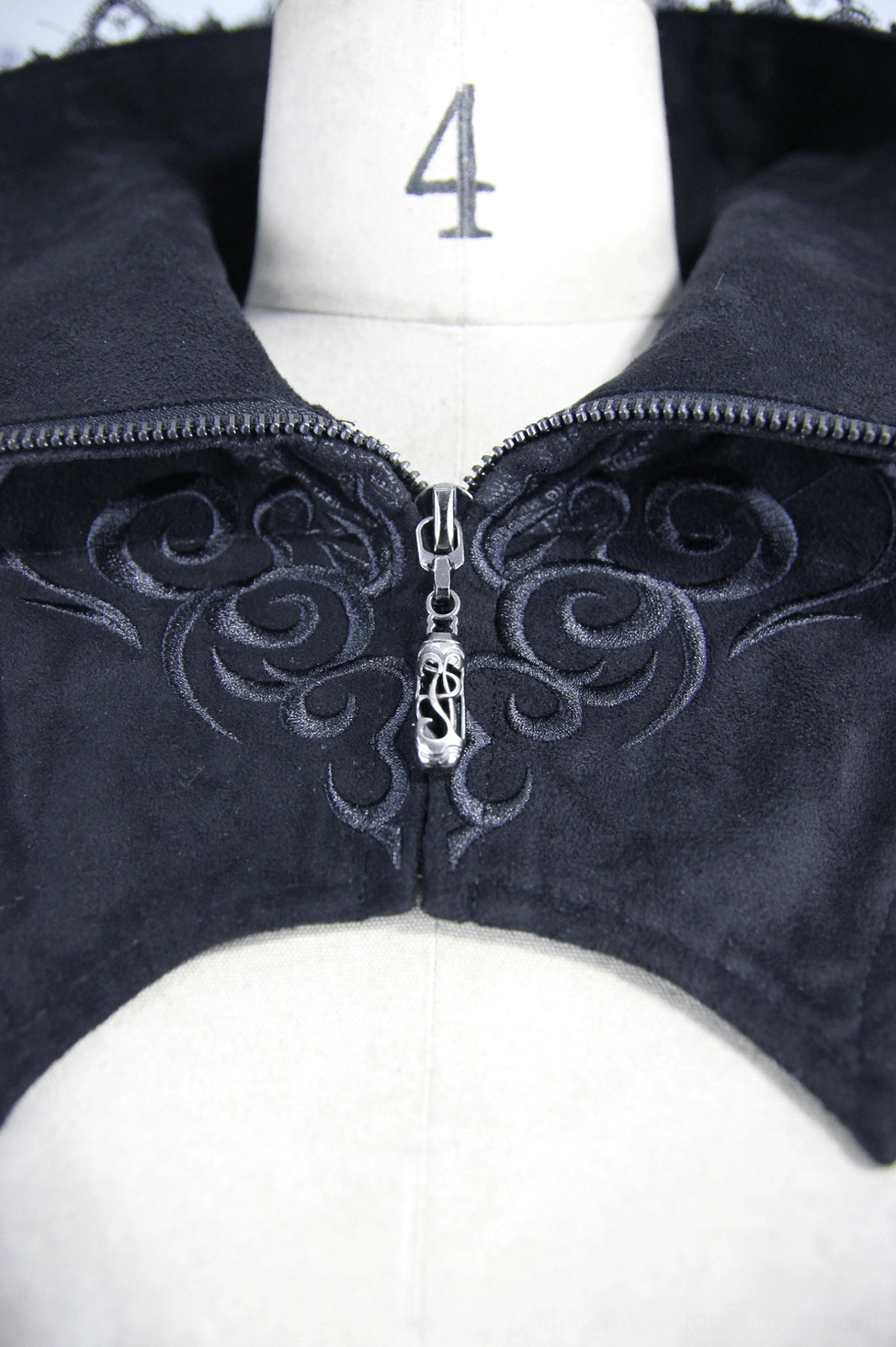 Close-up of gothic coat zipper showing ornate skull-shaped zipper pull and embroidered gothic motifs on black fabric