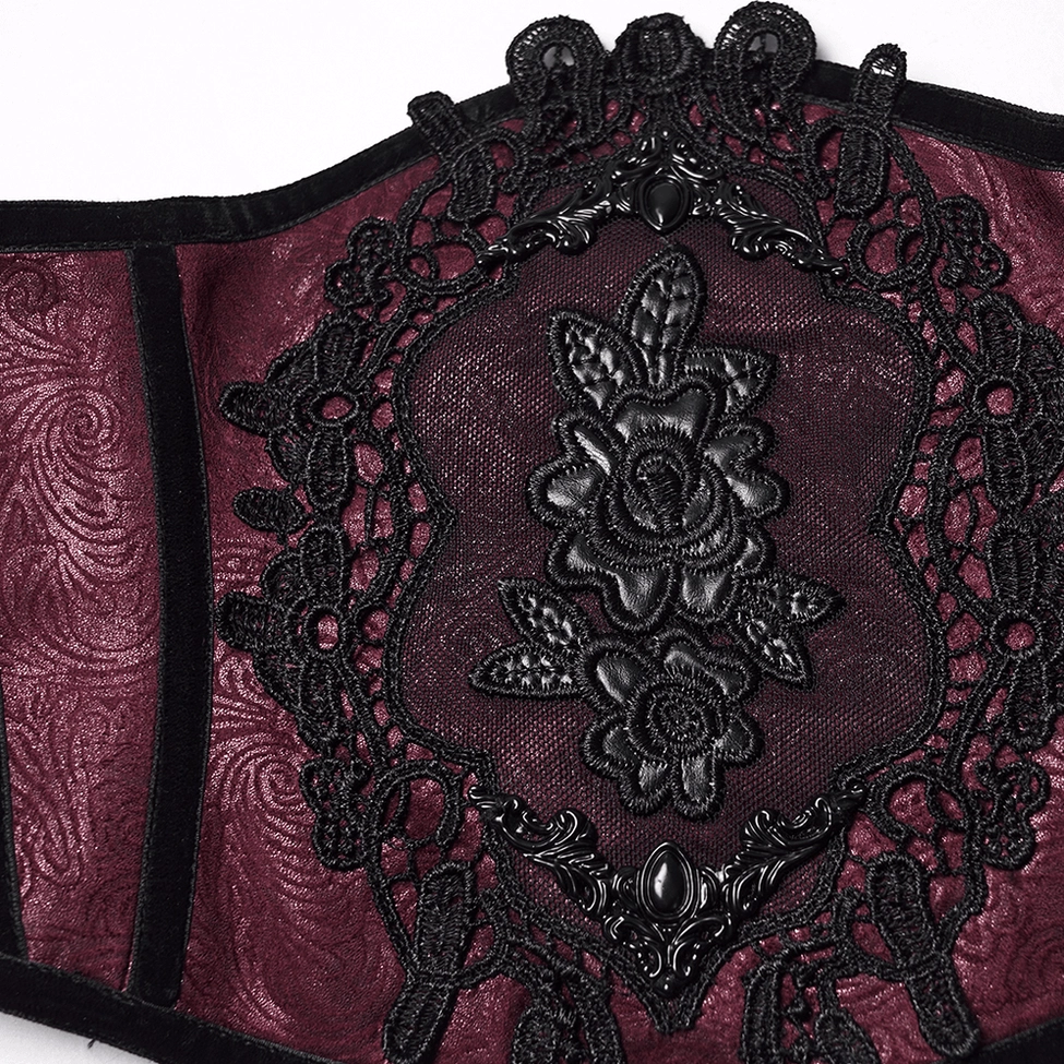 Close-up detail of ornate black lace applique with metal floral accents on wine red gothic corset belt