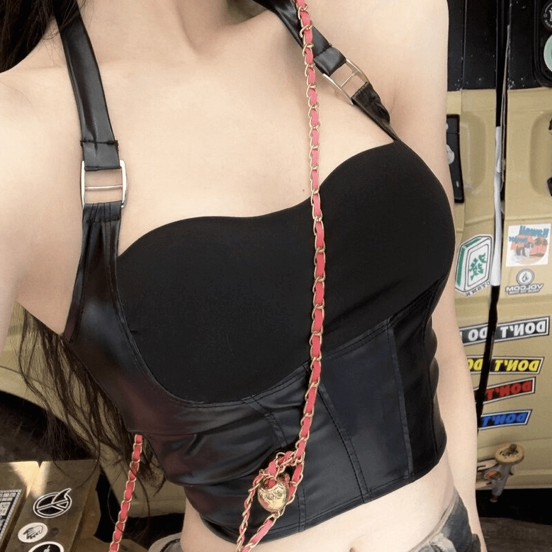 Black gothic corset-style crop top close-up showing adjustable buckle details, faux leather texture, and attached chain elements in retro garage setting