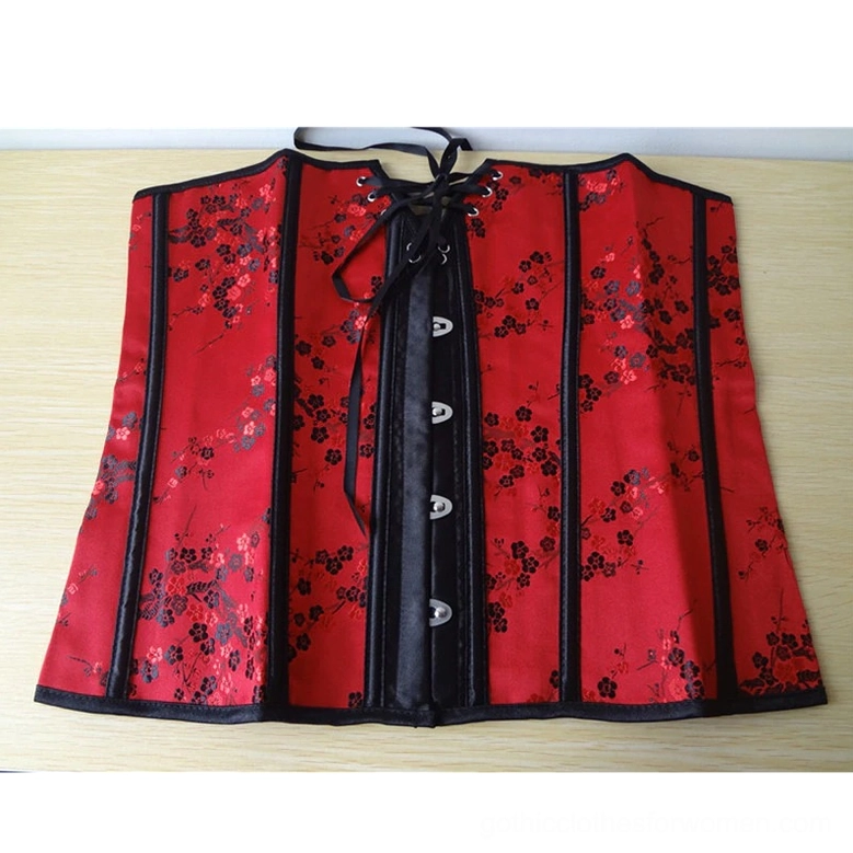 Red gothic corset flat lay top-down view showing front hook-and-eye fasteners, black floral satin fabric details on wooden background