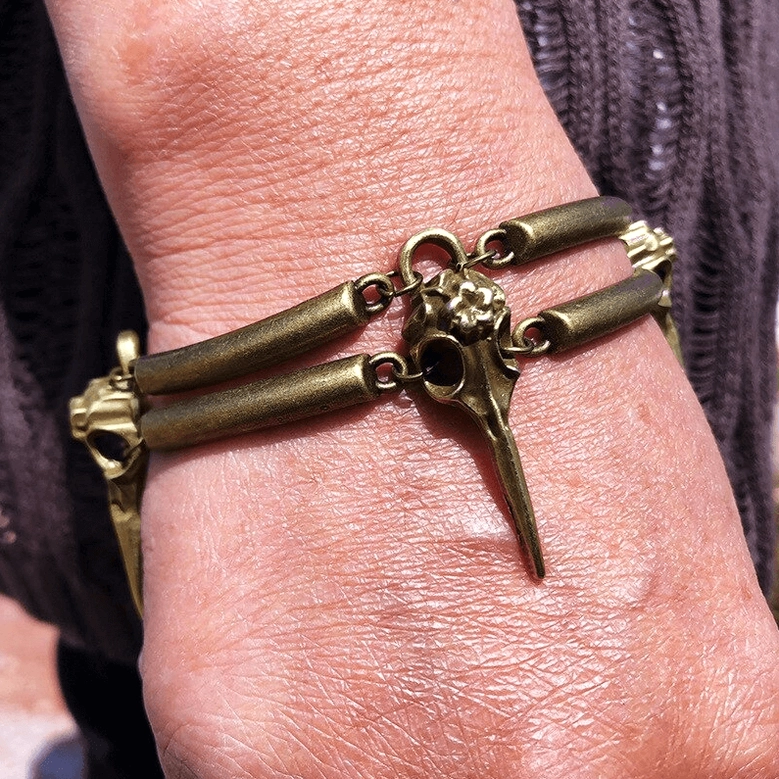 Crow skull antiqued bronze bracelet worn on back of hand, close-up showing fitted wrist wear over dark knit fabric