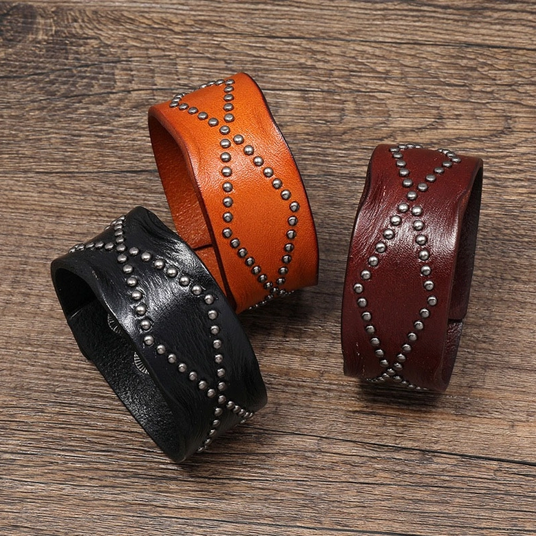 Three color variants of wide leather gothic cuff bracelets - black, brown, and wine red - displayed in flat lay overhead view on wooden surface