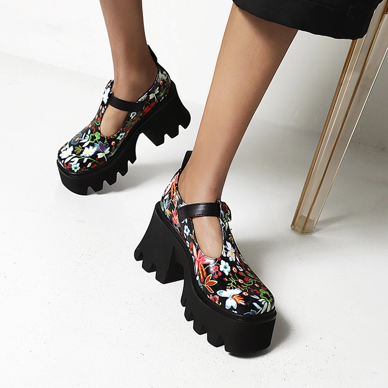 Woman wearing dark floral gothic platform Mary Jane pumps with black lug sole and T-strap, studio photo from low angle
