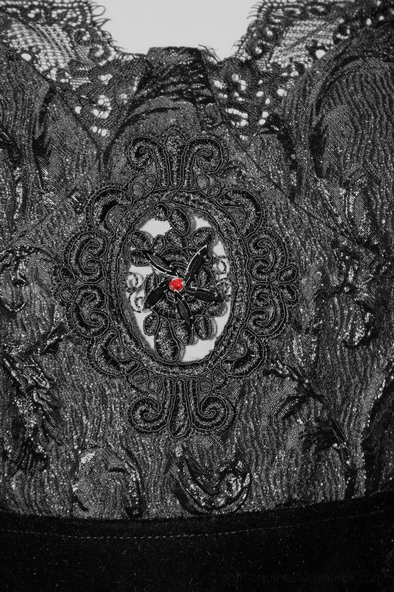 Close-up bust detail showing embossed floral lace pattern and striking red gemstone ornament on gothic dress centerpiece