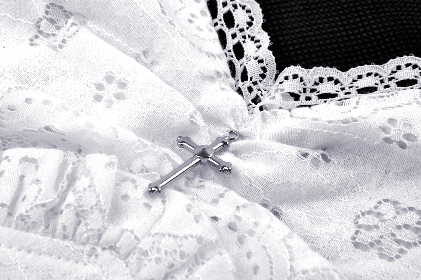 Close-up detail of white lace gothic dress showing cross metal decoration and intricate floral lace texture