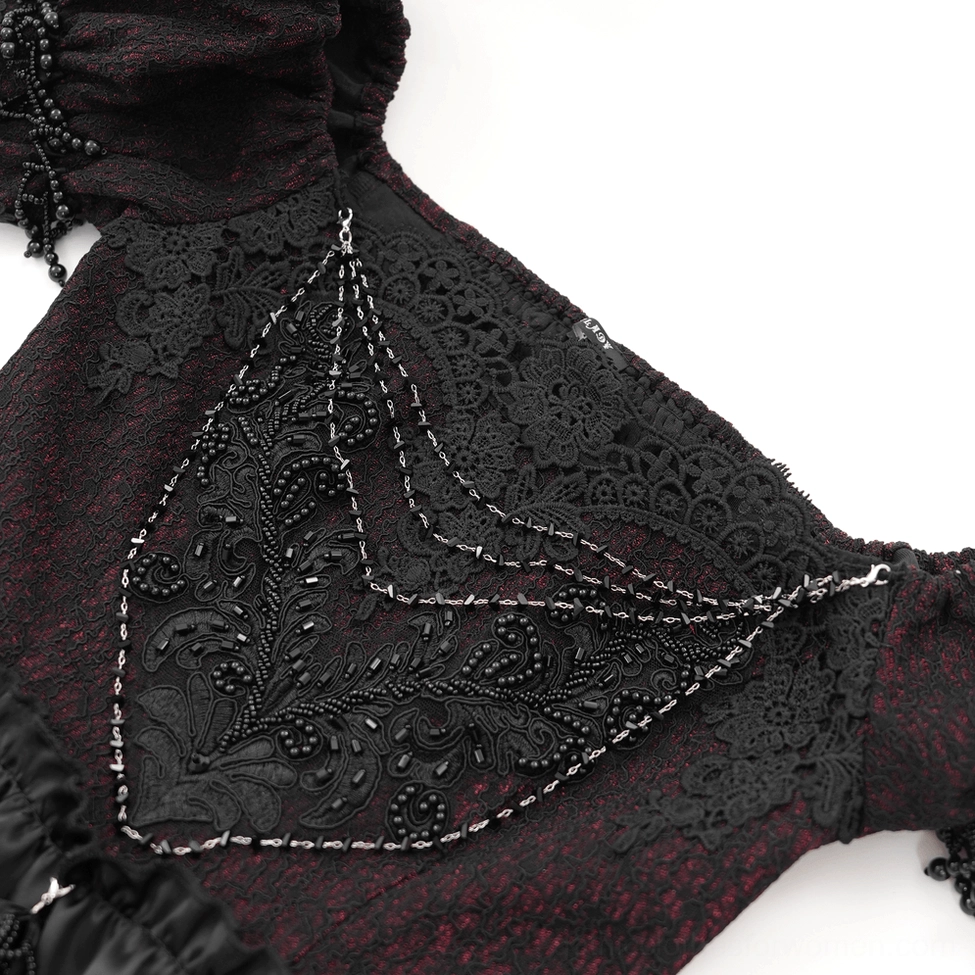 Close-up textile detail of gothic dress fabric showing black lace applique, ornate beaded chain trim, and velvet textured base material