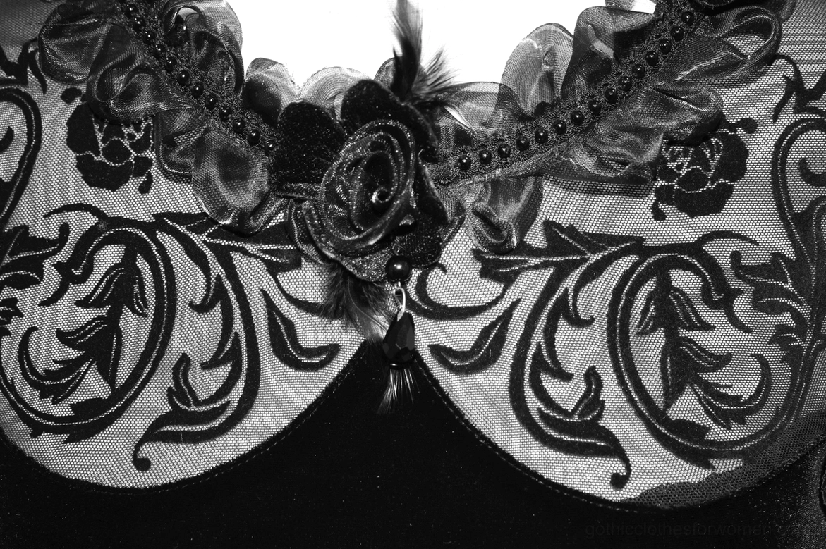 Close-up detail of filigree lace collar with floral pattern, fabric rose, and feather ornament