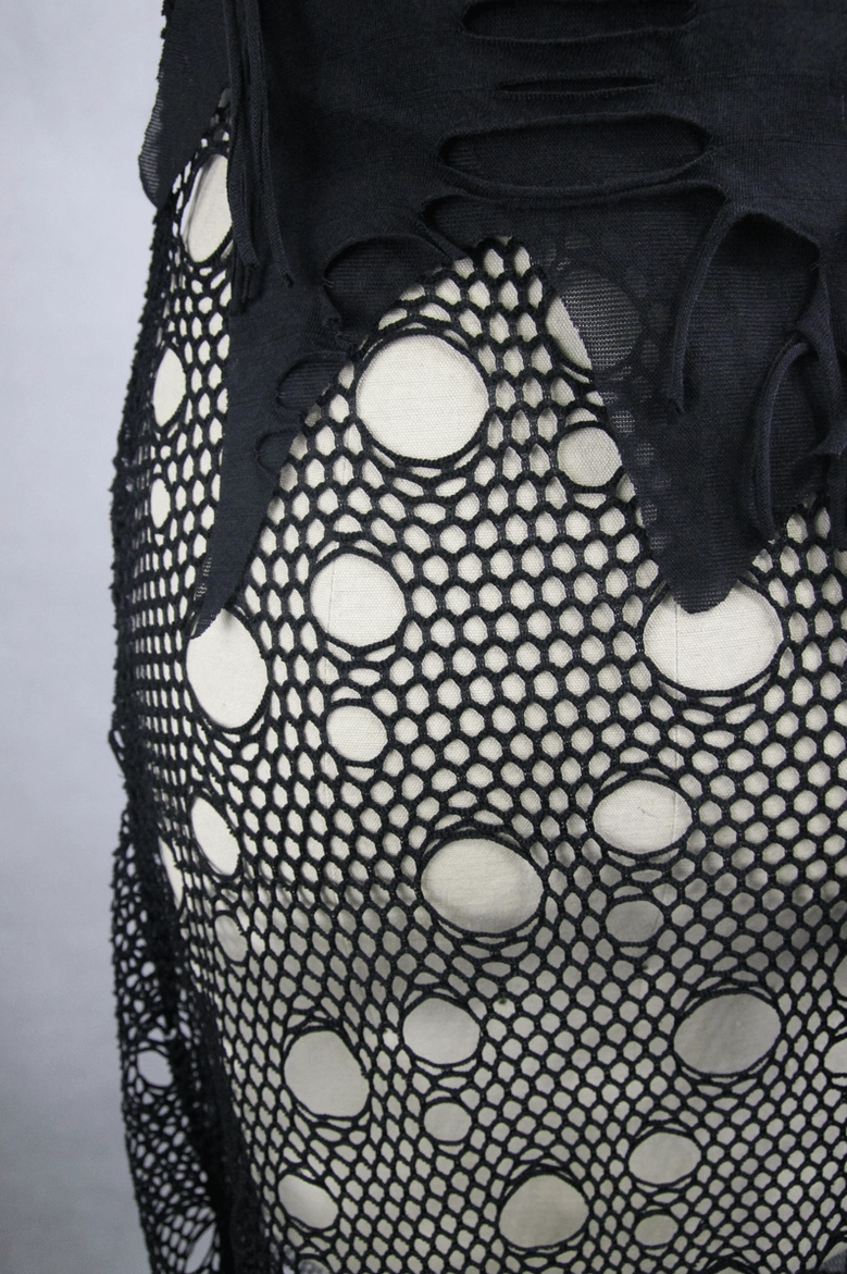 Close-up of distressed cutout hem and perforated fishnet fabric on black gothic dress skirt