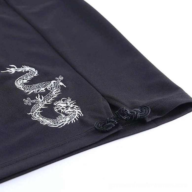 Flat lay detail of black gothic dress side panel showing white dragon embroidery and frog buttons
