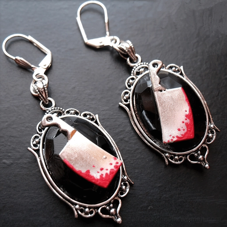 Side oblique angle view of blood-stained meat cleaver earrings showing red gem and vintage frame tilted display