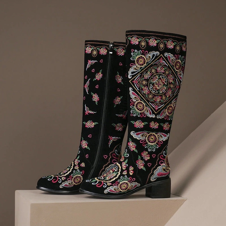 Pair of gothic knee-high boots with side zipper closure and full intricate embroidery, thick block heels front angle