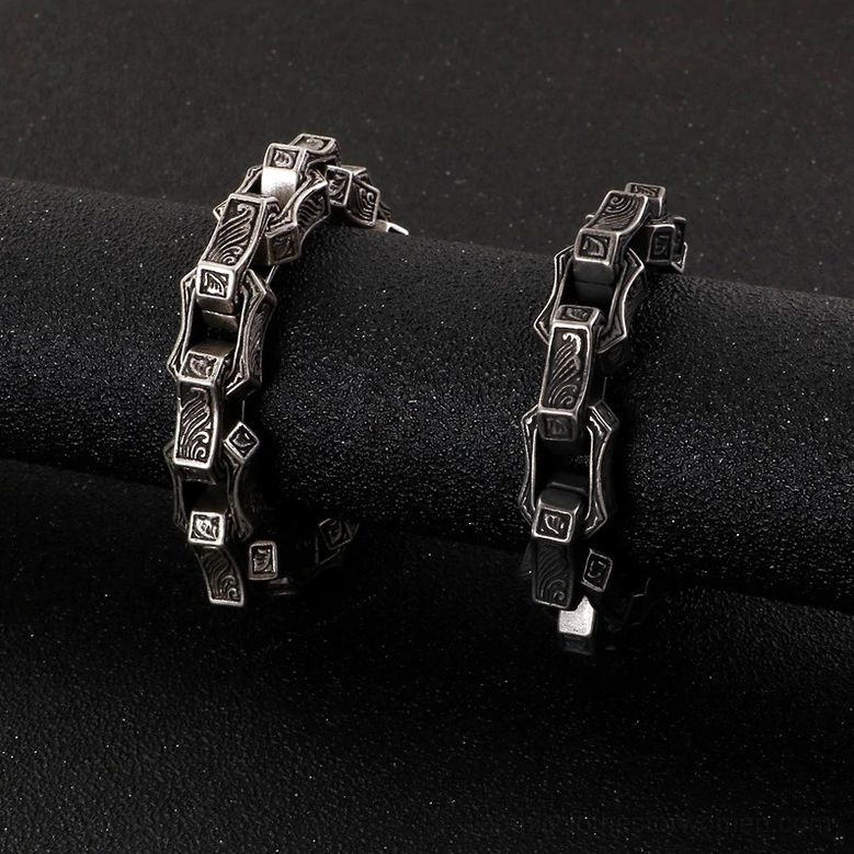 Two vintage gothic engraved stainless steel bracelets side by side dark grey studio background showing dual color tones