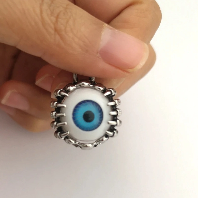 Close-up detail of gothic eyeball charm showing luminous blue iris and ornate spike-adorned surgical steel frame