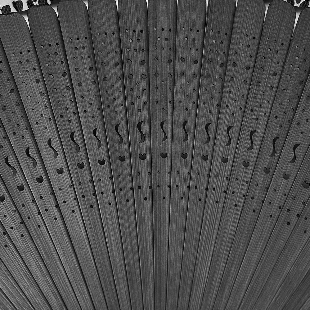 Close-up of hollow carved bamboo ribs on gothic fan, showing intricate decorative patterns in matte black finish