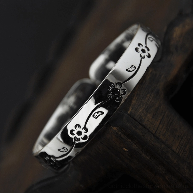 Two matching silver plated open cuff bangles with engraved floral patterns on dark wooden surface, showing gothic jewelry layering