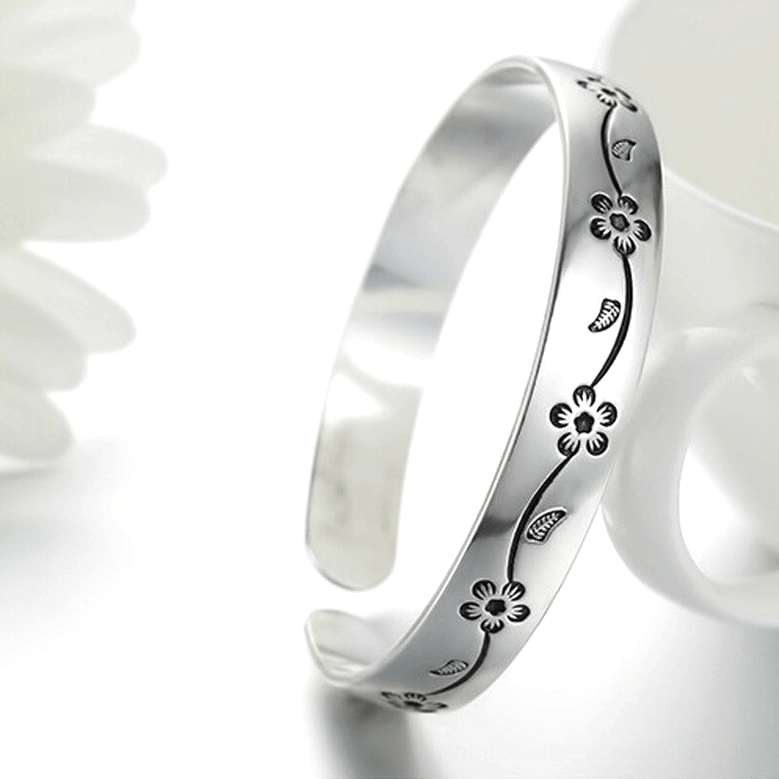 Silver plated gothic bangle with vintage flower vine engraving displayed on white ceramic cup, side angle view