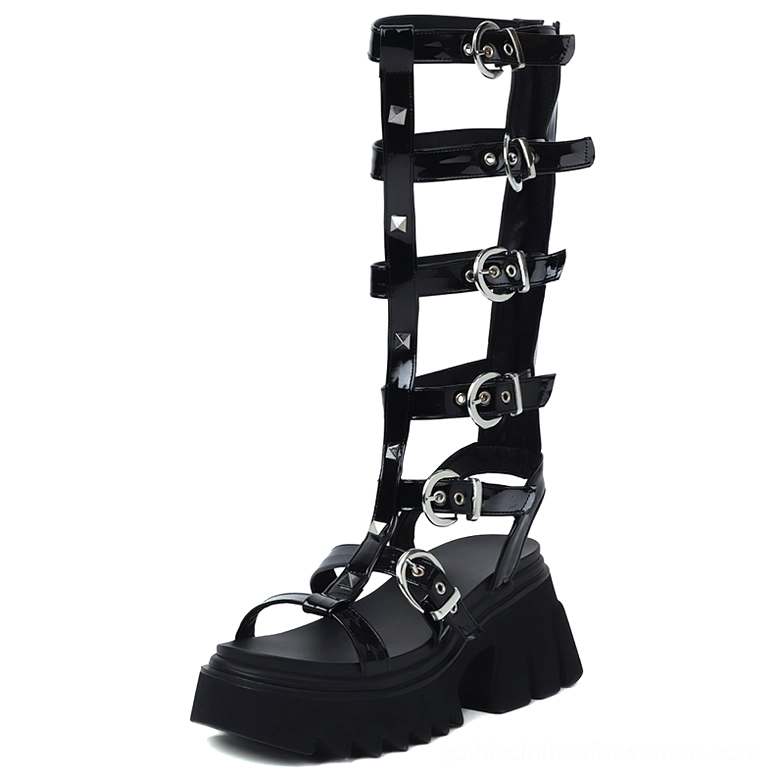 Black glossy leather knee-high gladiator platform sandals with silver pyramid studs and buckle straps, front left view studio photography