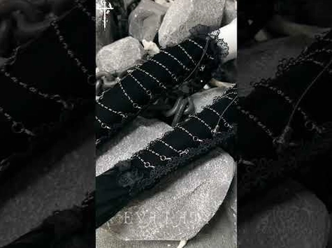 Close-up macro photography of gothic opera glove details featuring black velvet texture, metal chain patterns, and delicate lace trim on rocky background