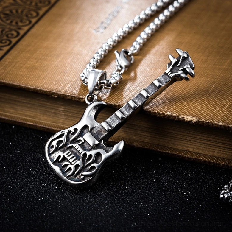Antique silver guitar pendant necklace styled on vintage book and dark surface showcasing gothic rock aesthetic