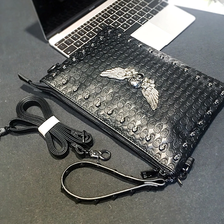 Alternative fashion black shoulder bag with detachable strap and skull embossing, styled on office desk with laptop