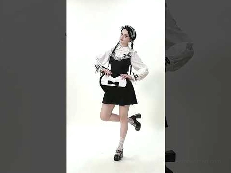 Full body model wearing black heart-shaped gothic lace bow crossbody bag with hands posed at bag waist in studio fashion shoot