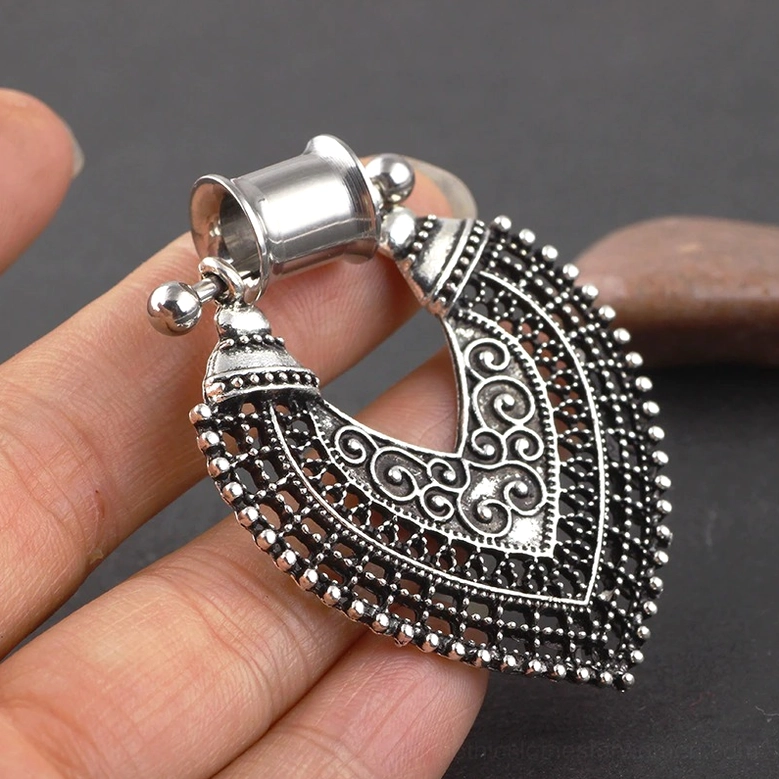 Close-up detail of vintage gothic heart ear tunnel held in hand showing scroll filigree pattern and beaded edge design