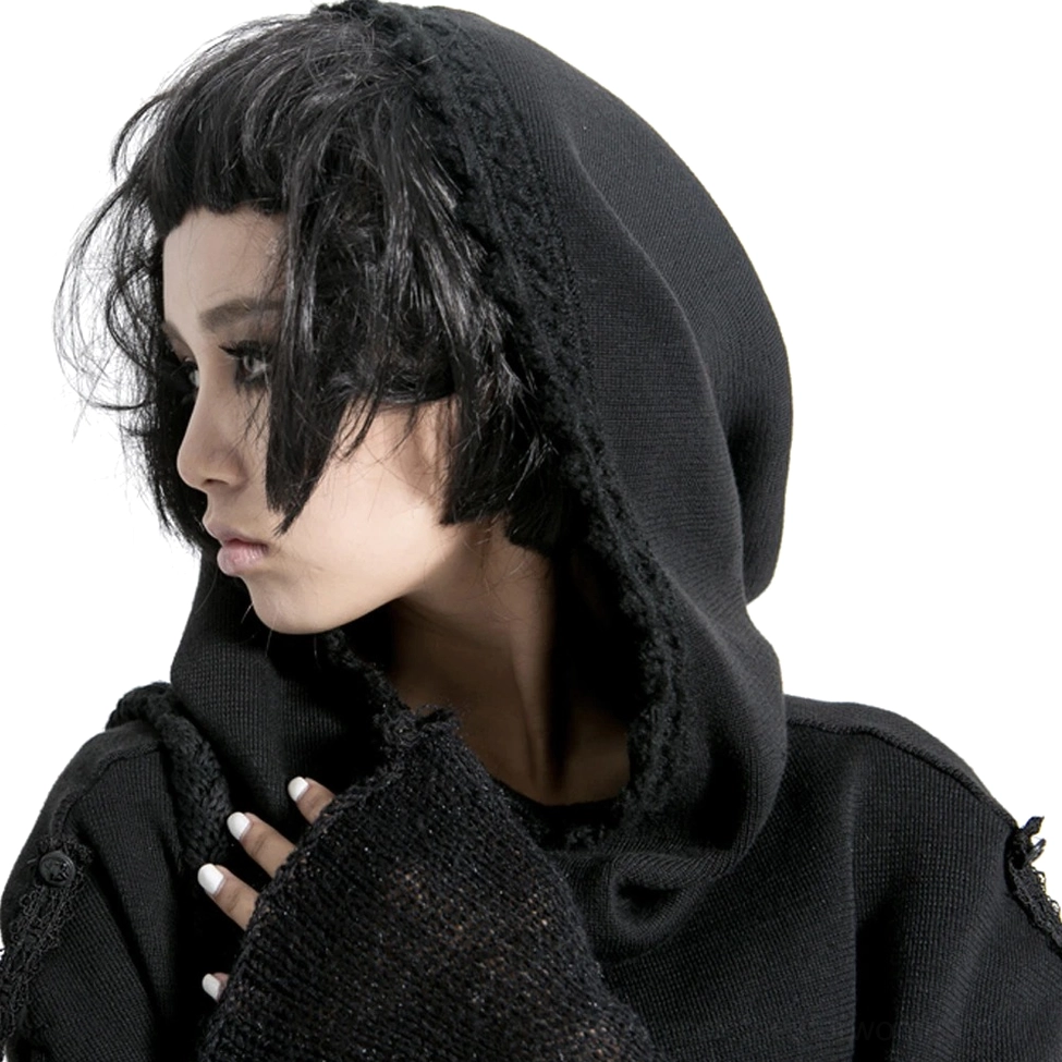 Close-up side profile of female model wearing hooded black knit cape showing frayed hood lining, fuzzy knit fabric texture, and button details