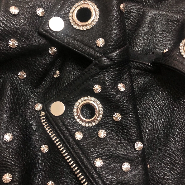 Close-up macro view of faux leather texture with star-shaped rivets and crystal-embellished grommets hardware