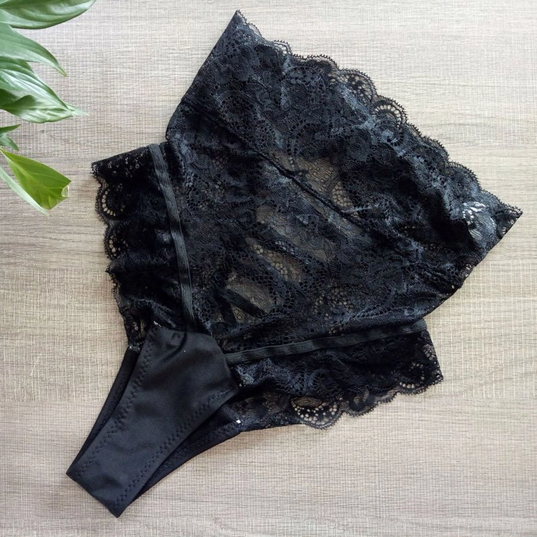 Black gothic lace underwear with scalloped lace trim detail, side view on wooden surface with green plants
