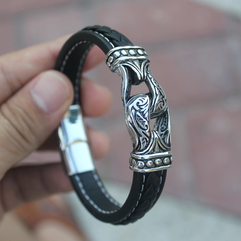 Hand-held side view of black leather gothic bracelet with ornate stainless steel buckle, indoor display