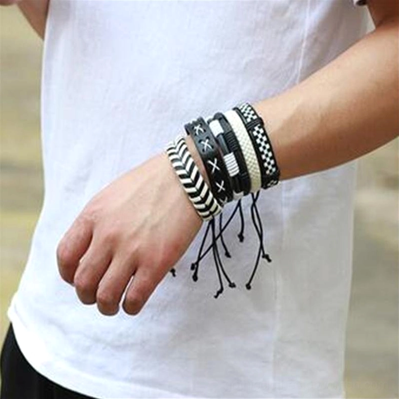 Male wrist wearing stacked black and white gothic leather bracelets with geometric patterns and tassel cord details