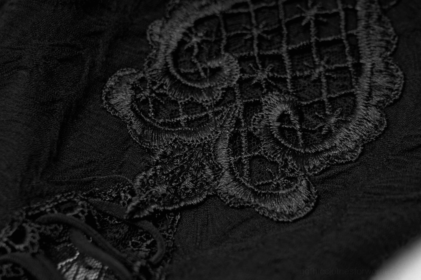 Detailed close-up of matte black fabric with vintage embroidered lace appliqué decoration on gothic leg warmer