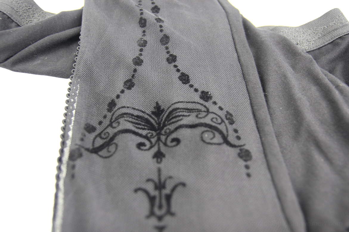 Close-up detail of baroque print on black mesh overlay, showing intricate chain and scroll pattern texture on gothic leggings