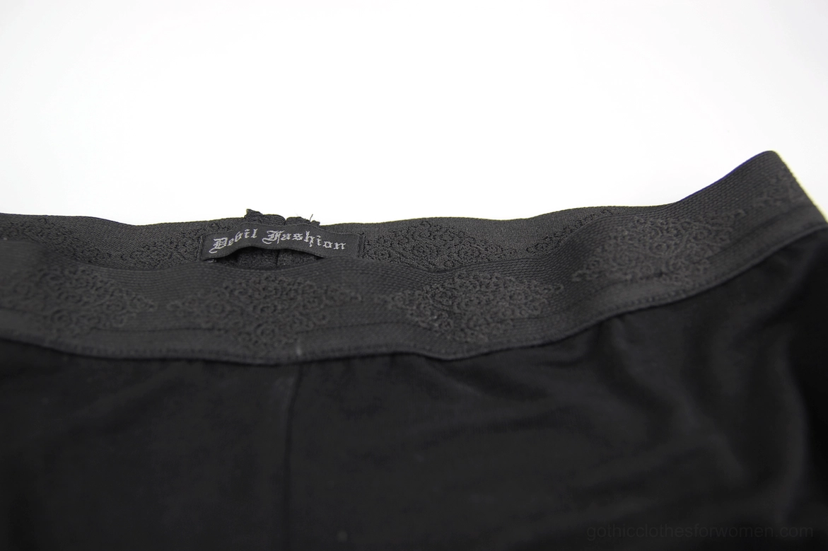Waistband detail of gothic mesh leggings, showing elastic black band and brand label attachment on top-down view