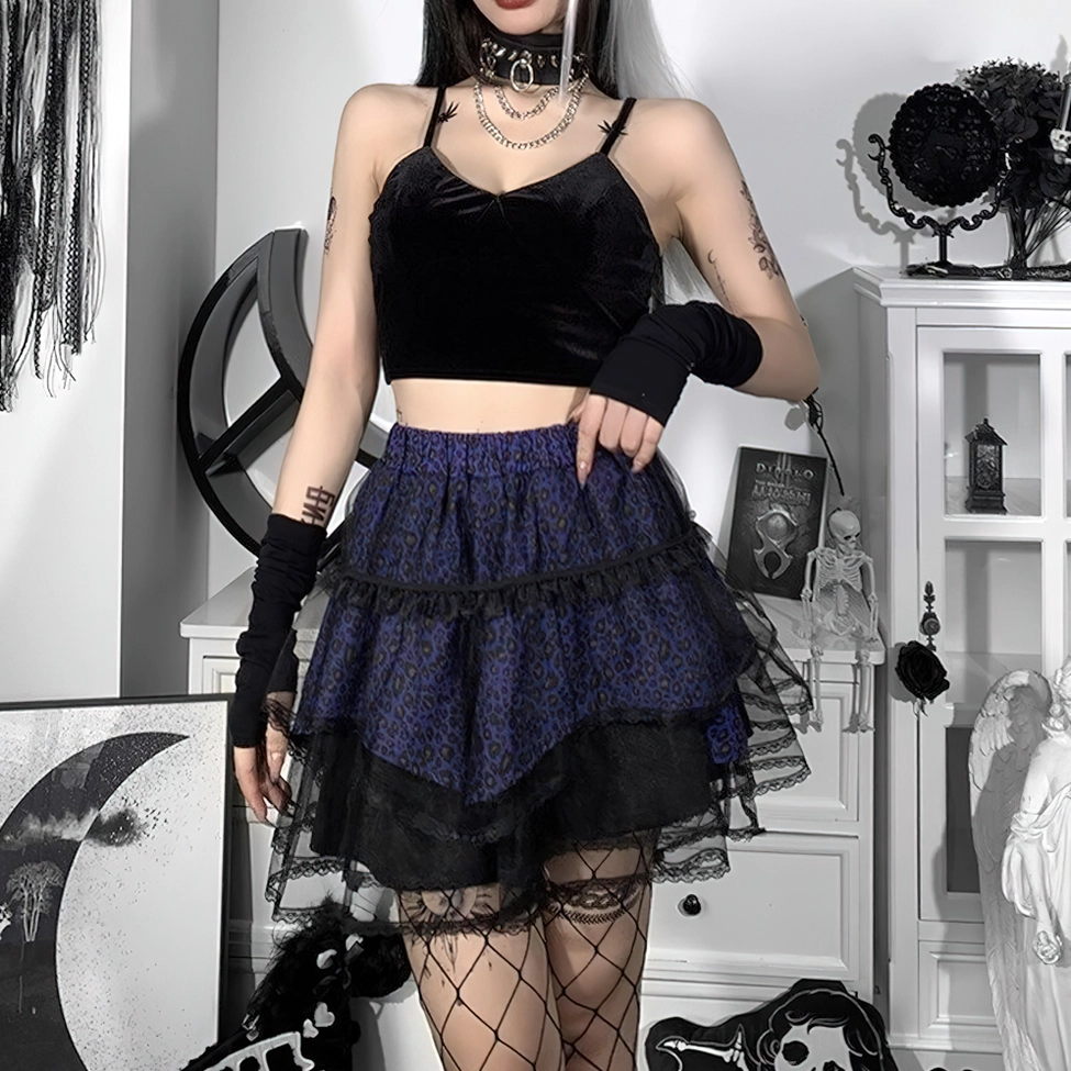 Tattooed model wearing purple leopard gothic skirt with black crop top and fishnet stockings in dark gothic studio