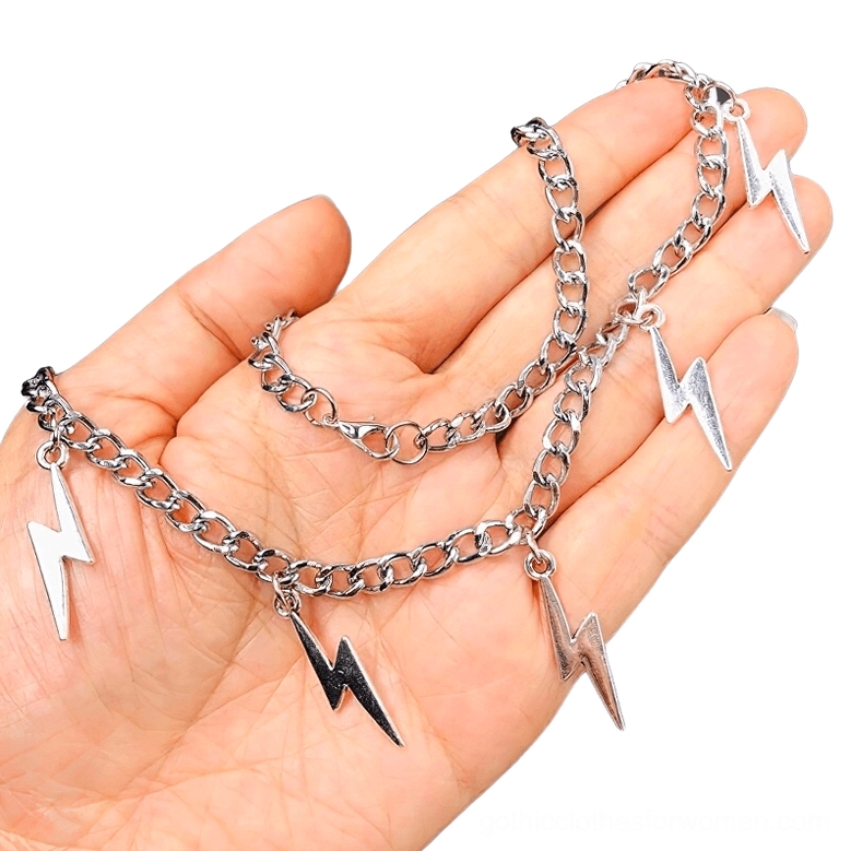 Close-up detail of silver and gunmetal lightning charm pendants held in palm, showing intricate geometric design and craftsmanship