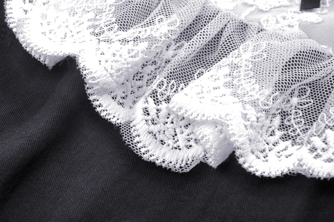 Close-up of dress trim showing white lace ruffle detail and solid black woven fabric construction