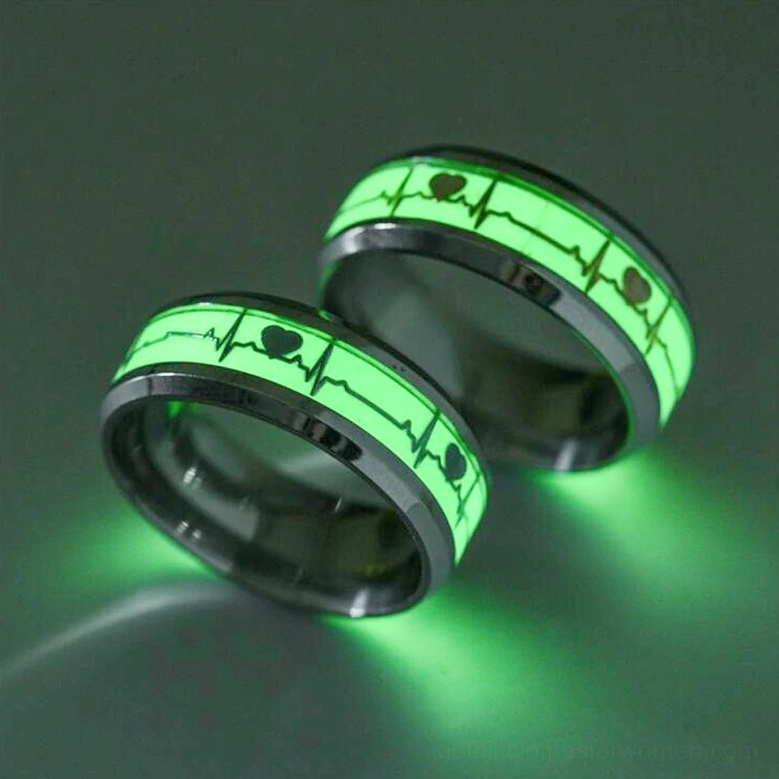 Black stainless steel luminous ECG heartbeat ring pair, low oblique view on dark reflective background with bright green glowing heart pattern