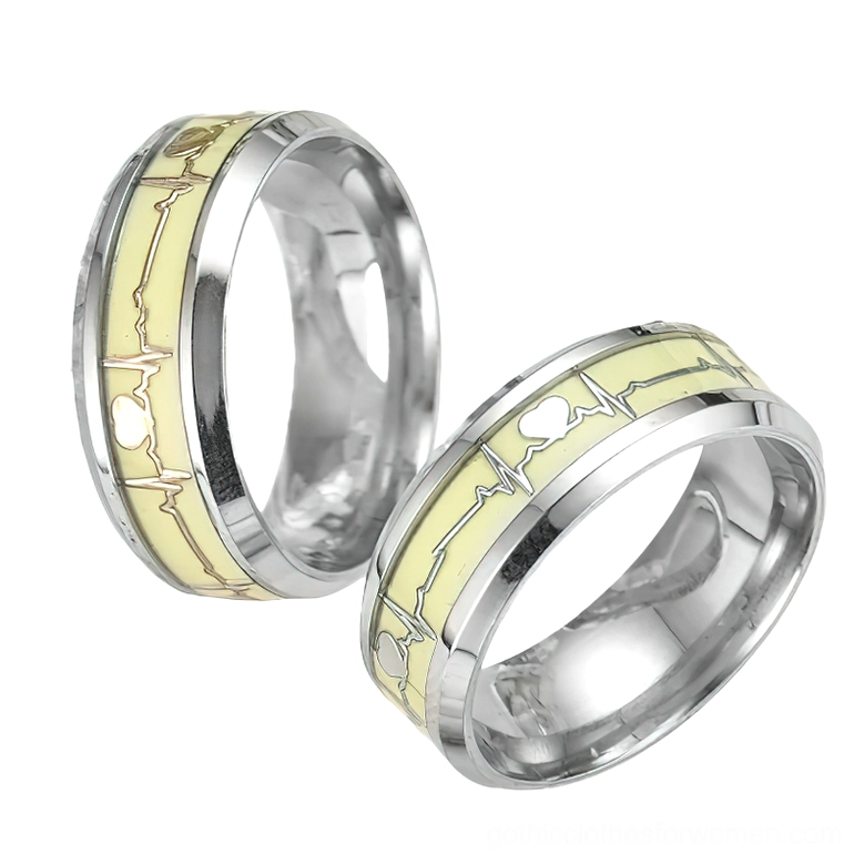 Luminous ECG heartbeat ring pair, low angle view showing polished silver stainless steel bands with gold-toned glowing heart and waveform inlay