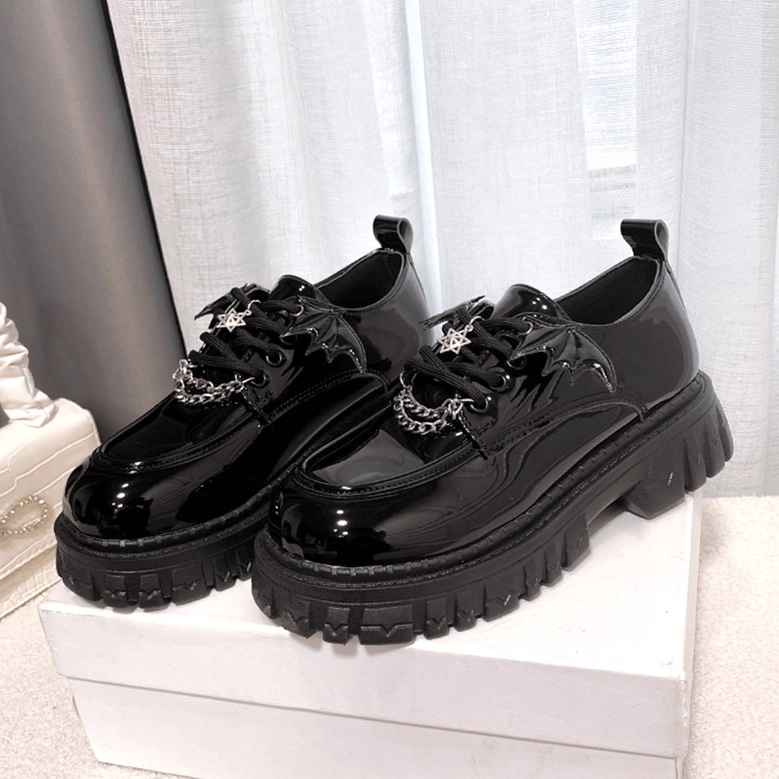 Pair of black patent leather gothic platform loafers with shiny finish and metal ornaments, front-side angled view on display