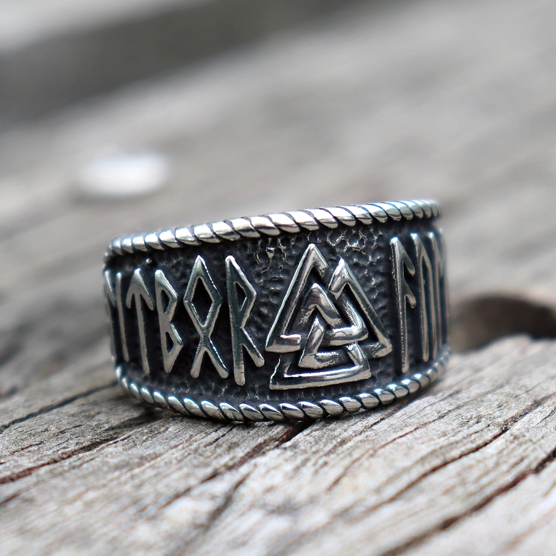 Gothic Norse rune ring featuring dark silver patina, twisted rope edge, and Valknut symbol patterns on rustic wooden plank background