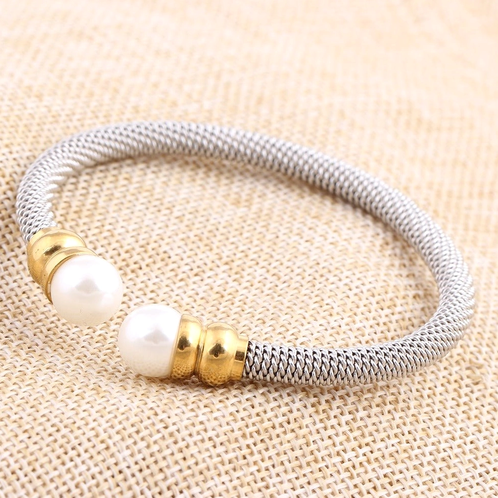 Open bangle cuff pearl bracelet on studio metal sheet background emphasizing stainless steel craftsmanship
