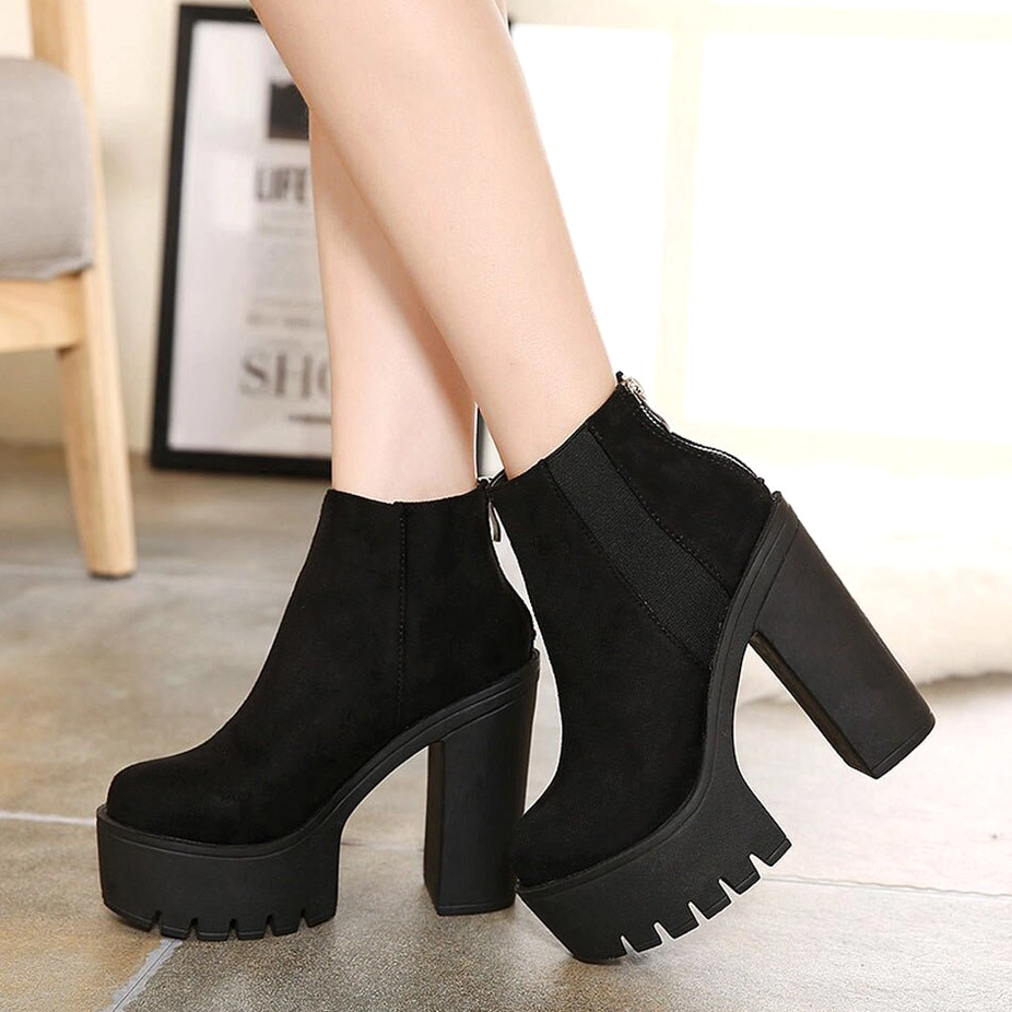 Black gothic platform ankle boots worn on female model in indoor setting, side three-quarter view of chunky heel and platform