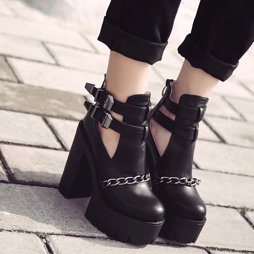 Black gothic platform boots worn on model's feet from low angle showing chunky block heels and outdoor street scene
