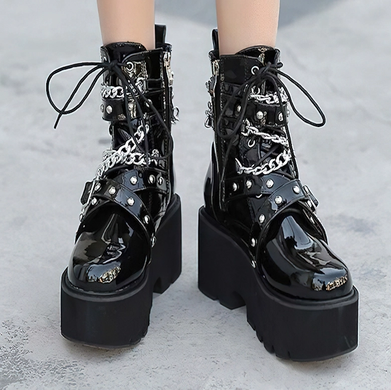 Woman wearing black gothic platform boots outdoors on concrete, front low angle showcasing chain decorations and industrial aesthetic