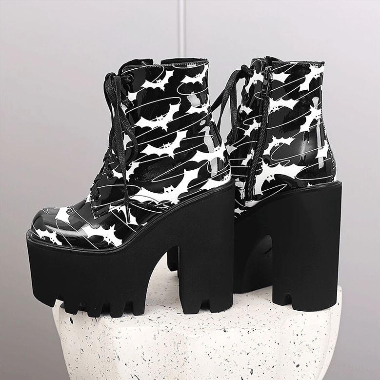 Pair of gothic platform ankle boots with bat wing print and black thick platform soles on white stone stand, side and rear view showing collar pull tabs