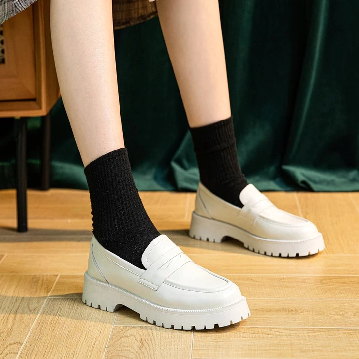 White platform loafers styled on female model with black socks and plaid skirt, low-angle front view on wooden floor